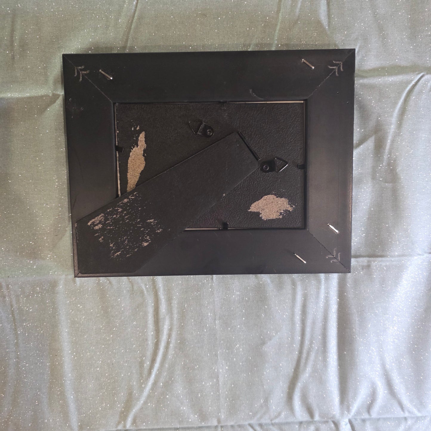 Black picture frame with peeling paint on a textured light gray surface